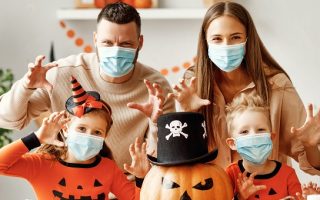 Familia celebrando halloween en casa en plena pandemia de coronavirus. Con una calabaza grande decorada también con mascarilla. Niños con pijama o disfraz de calabaza de color naranja.