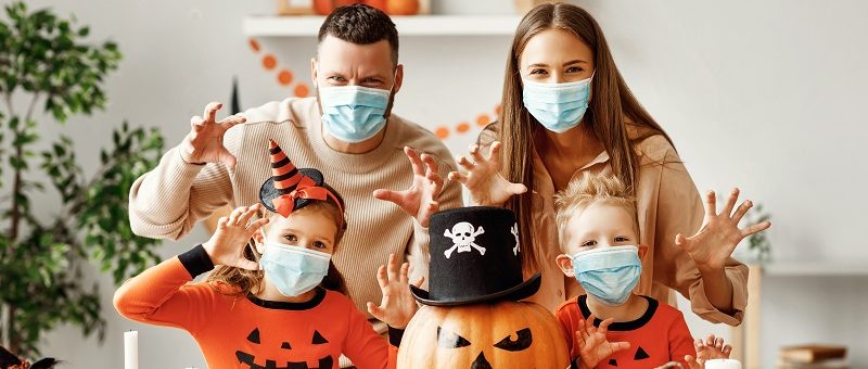 Familia celebrando halloween en casa en plena pandemia de coronavirus. Con una calabaza grande decorada también con mascarilla. Niños con pijama o disfraz de calabaza de color naranja.