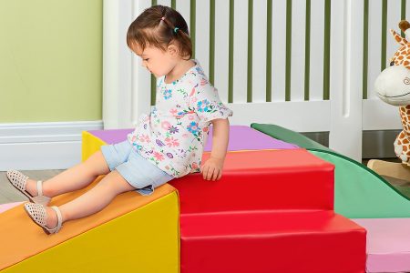 Niña jugando con bloques de espuma y al lado hay un balancín infantil en forma de jirafa