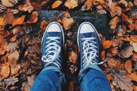 Primer plano de unos pies con zapatillas sobre un suelo mojado lleno de hojas en otoño