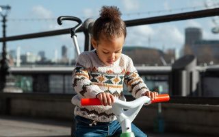 niña montada en un triciclo infantil con barra de empuje disfrutando al aire libre