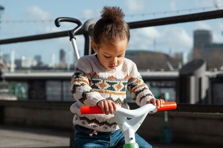 niña montada en un triciclo infantil con barra de empuje disfrutando al aire libre