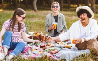 3 chicas haciendo un picnic en el campo junto a un perrito de color blanco