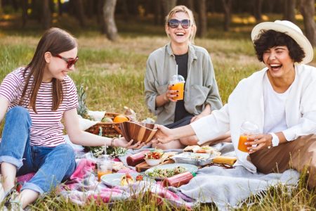 3 chicas haciendo un picnic en el campo junto a un perrito de color blanco