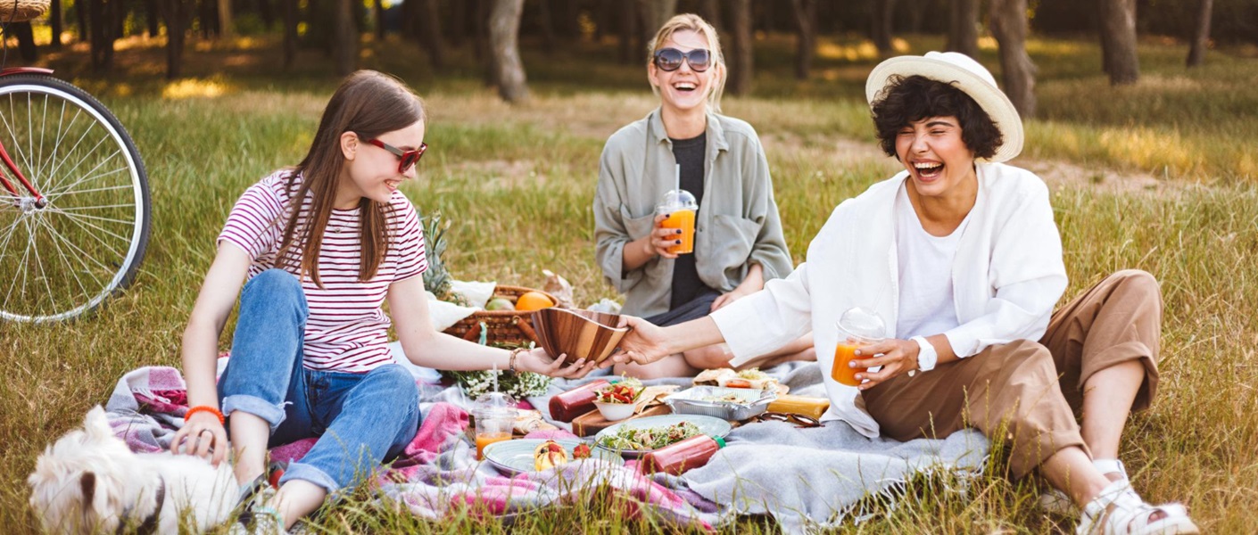 3 chicas haciendo un picnic en el campo junto a un perrito de color blanco