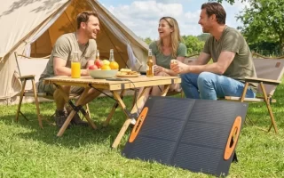Grupo de amigos disfrutando al aire libre con un panel solar portátil desplegado frente a su carpa