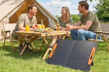 Grupo de amigos disfrutando al aire libre con un panel solar portátil desplegado frente a su carpa
