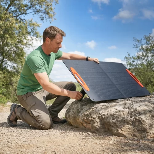 Hombre ajustando el ángulo de un panel solar portátil apoyado sobre una roca en el aire libre