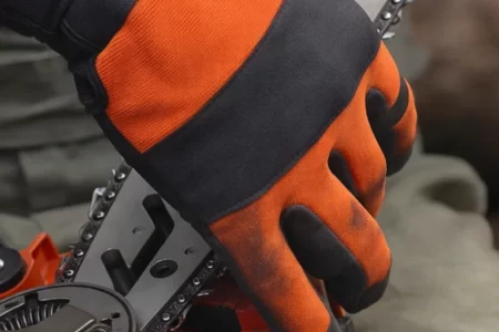 Manos con guantes naranjas y negros colocando la cadena en la espada de una motosierra eléctric