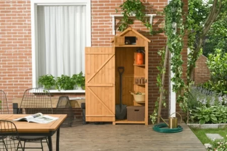 Armario de madera natural tipo cobertizo con puerta abierta junto a una terraza con mesa y sillas