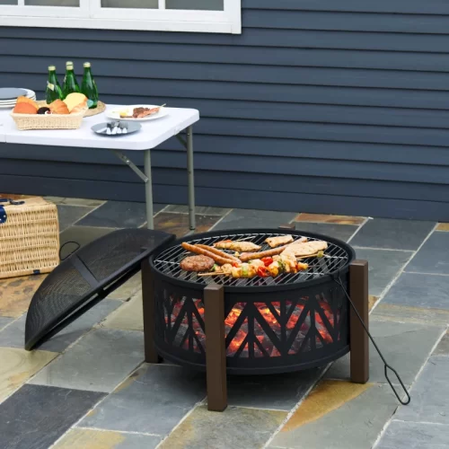 Brasero tipo cuenco con parrilla asando carne y verduras junto a una mesa con aperitivos en el jardín
