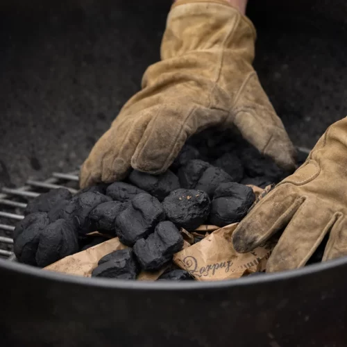 Manos con guantes colocando briquetas de carbón en pirámide