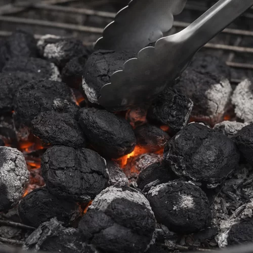 Pinzas moviendo briquetas de carbón caliente en la parrilla