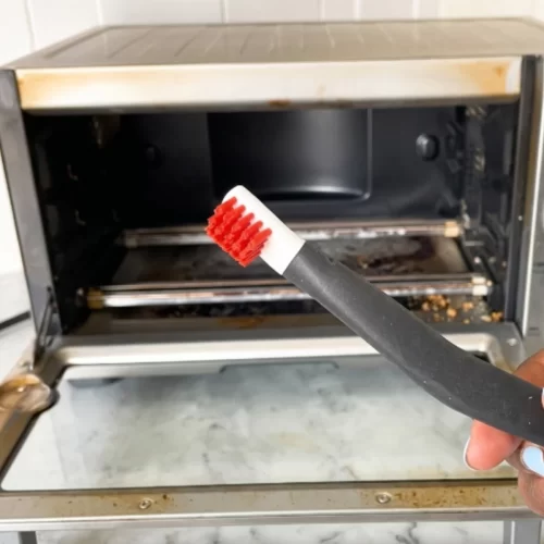 Cepillo de detalle limpiando las esquinas de un horno tostador abierto y sucio.