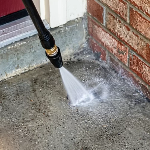 Chorro de agua a presión limpiando un suelo de hormigón junto a una pared de ladrillo