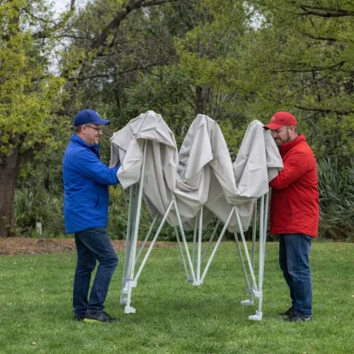 Dos personas plegando una carpa gazebo caminando hacia el centro de la estructura
