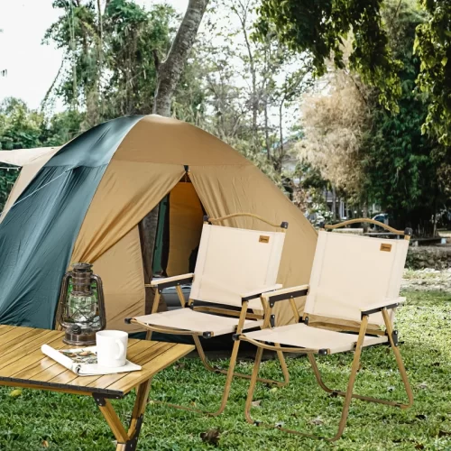 Dos sillas de camping plegables de madera junto a una tienda de campaña y mesa auxiliar