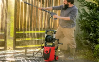 Hombre usando una hidrolimpiadora eléctrica roja con carrete de manguera para limpiar una va