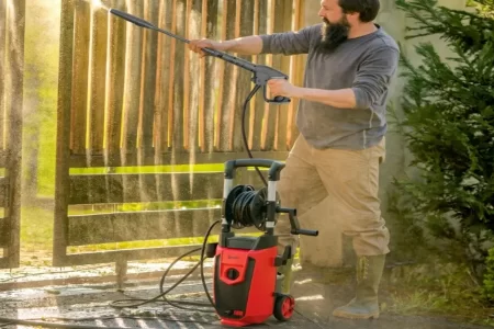 Hombre usando una hidrolimpiadora eléctrica roja con carrete de manguera para limpiar una va