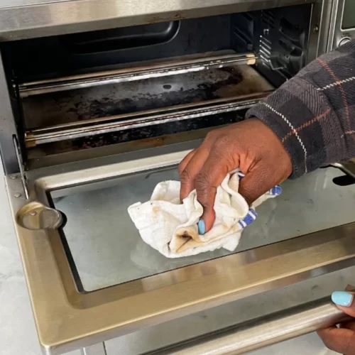 Limpiando la puerta de vidrio del horno tostador con un trapo húmedo.