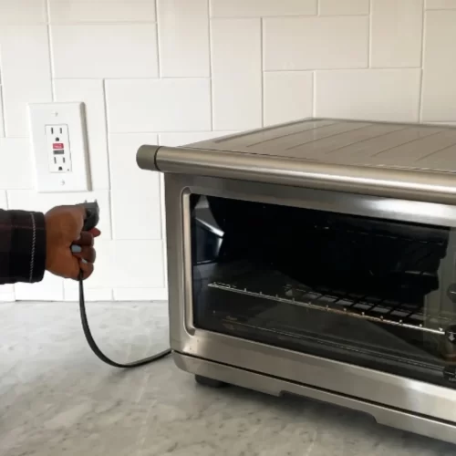 Mano desenchufando el horno tostador de la toma de corriente.
