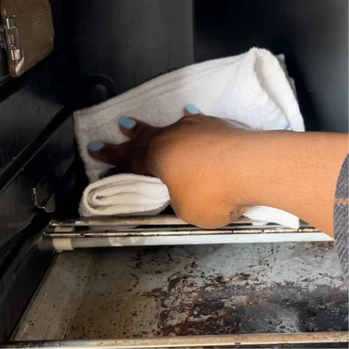 Mano limpiando el interior sucio del horno tostador con un trapo blanco.