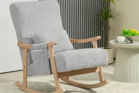 Mecedora tapizada en gris con reposabrazos de madera y cojín lumbar en el saló