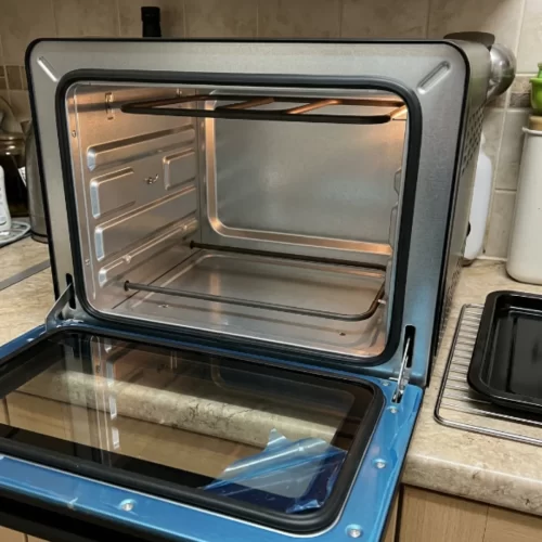 Mini horno vacío con la puerta de cristal abierta, con las resistencias a la vista, junto a la bandeja y la rejilla.