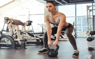 Mujer en gimnasio realizando peso muerto con kettlebell negra de 8 kg 1400