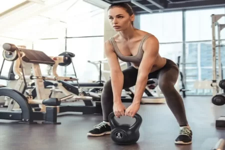Mujer en gimnasio realizando peso muerto con kettlebell negra de 8 kg 1400