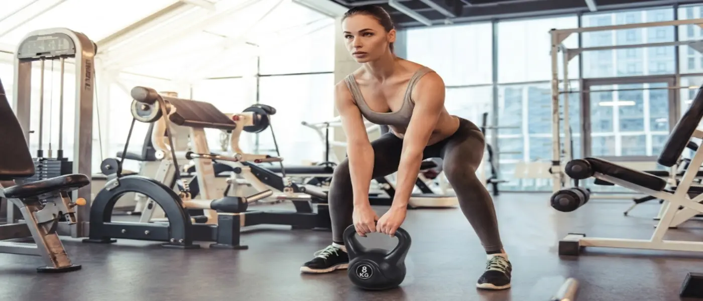 Mujer en gimnasio realizando peso muerto con kettlebell negra de 8 kg 1400