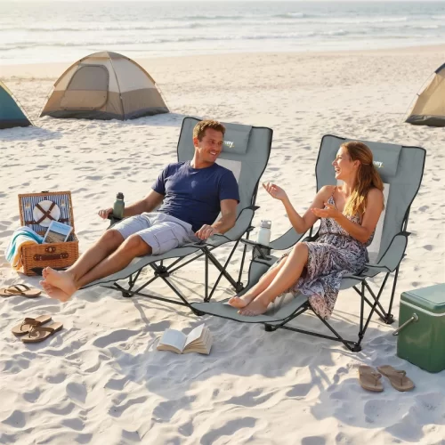 Pareja relajada en sillas de camping reclinables con reposapiés en la playa, junto a tiendas de campaña y nevera portátil