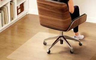 Persona sentada en una silla de oficina sobre una alfombrilla transparente antideslizante en suelo de madera. 1400