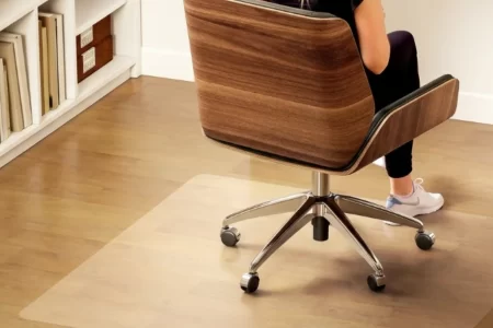 Persona sentada en una silla de oficina sobre una alfombrilla transparente antideslizante en suelo de madera. 1400