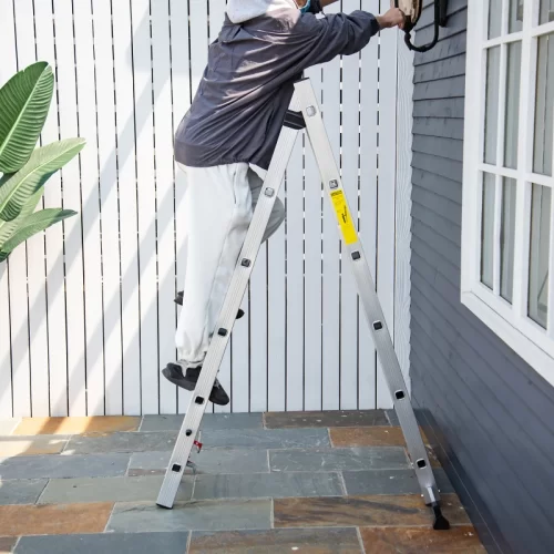 Persona subida a una escalera de tijera de aluminio realizando trabajos de mantenimiento en el exterior