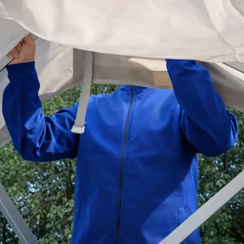 Persona sujetando la hebilla de la lona bajo el techo de una carpa gazebo