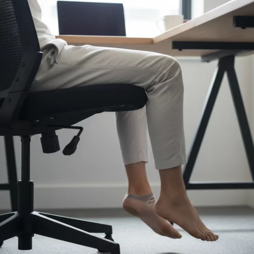 Pies colgando sin apoyo bajo un escritorio de oficina