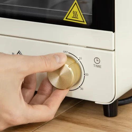 Primer plano de una mano girando el mando dorado del temporizador de un mini horno crema, marcado en OFF, 10, 20 y 30 minutos.