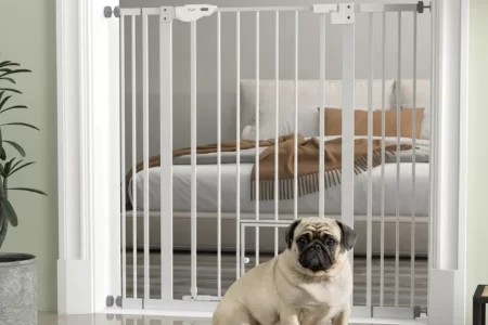 Puerta de seguridad blanca con puertita para mascotas y un pug sentado frente a ella. 1400