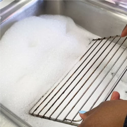 Rejilla del horno remojándose en agua jabonosa dentro del fregadero.