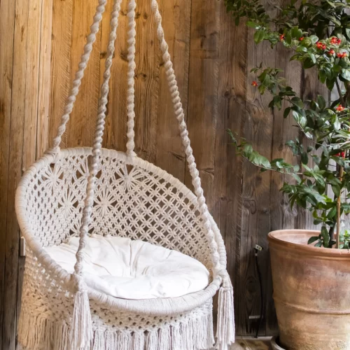 Silla colgante de macramé terminada con flecos y cojín en terraza rústica de madera
