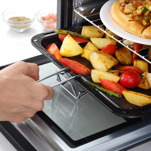 Mano retirando bandeja de verduras asadas de un horno de sobremesa.